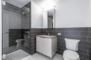 Unit Bathroom, glass shower door, no bathtub, mirrored vanity with storage, sink with storage underneath, tile floor, dark subway tile on walls.