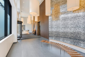Interior entrance lobby, contemporary art and furniture throughout room, large overhead lighting installation, large contemporary black and white wall behind bench, Revolving Doors, large 7 dekalb signage at entrance, wood walls near elevator, front desk to the left of entrance.
