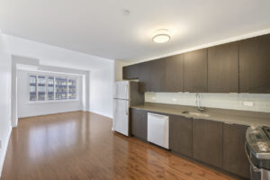 Interior Unit Kitchen, wood floors, dark brown cabinetry, stone countertops, stainless steel appliances, living room opposite side of room, large window in living room.