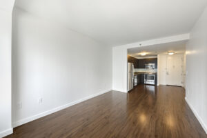 Interior Unit Living Room, wood floors, stainless steel appliances in kitchen area, open floor plan, white walls.