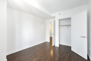 Interior unit bedroom, wood floors, white walls, closet parallel to window.
