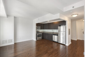 Interior Unit Living Room, Open floor plan, stainless steel appliances, stone countertop, dark brown cabinets, white wall.