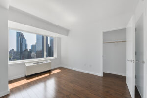Interior Unit Bedroom, AC unit near window, view of downtown in bedroom, wood floors, closet next to entrance.