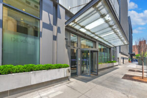 Exterior Entrance of 7 Dekalb, planters with bushes on both sides of entrance, revolving entrance door, covered entrance.