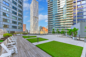 Exterior Rooftop area, lounge chairs around rooftop, grass patches, garden area, view of surrounding buildings, seated courtyard area, photo taken on a sunny day with clouds.